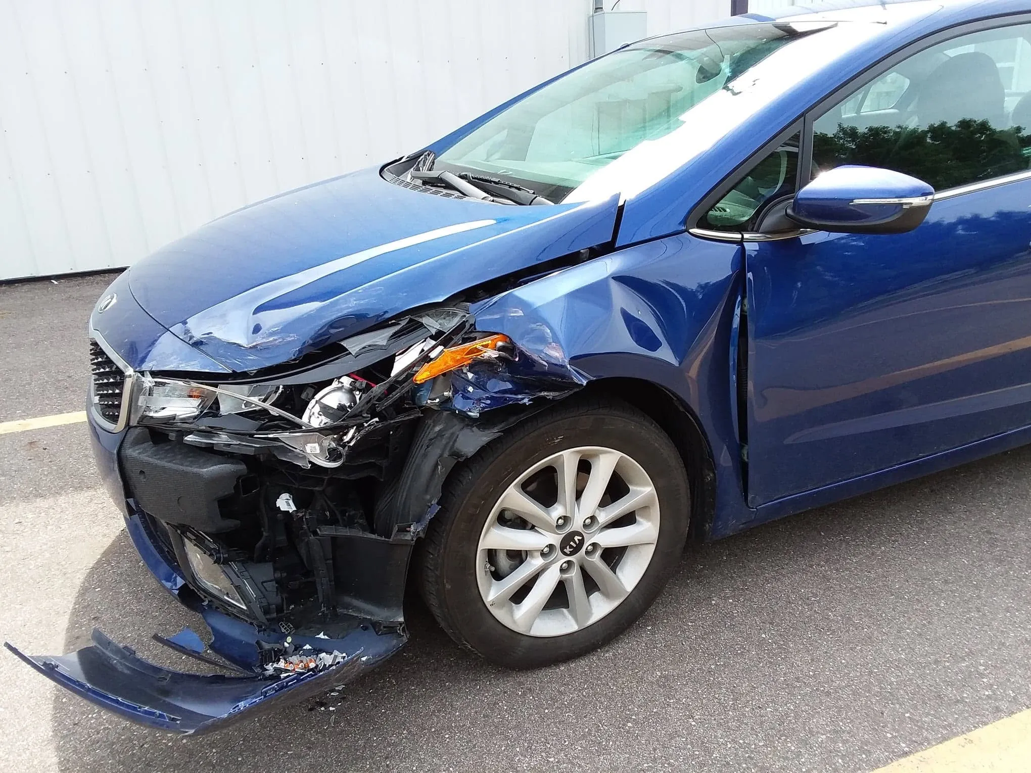 Blue Kia Forte with front-end collision damage — bumper, headlight, fender and wheel arch destroyed